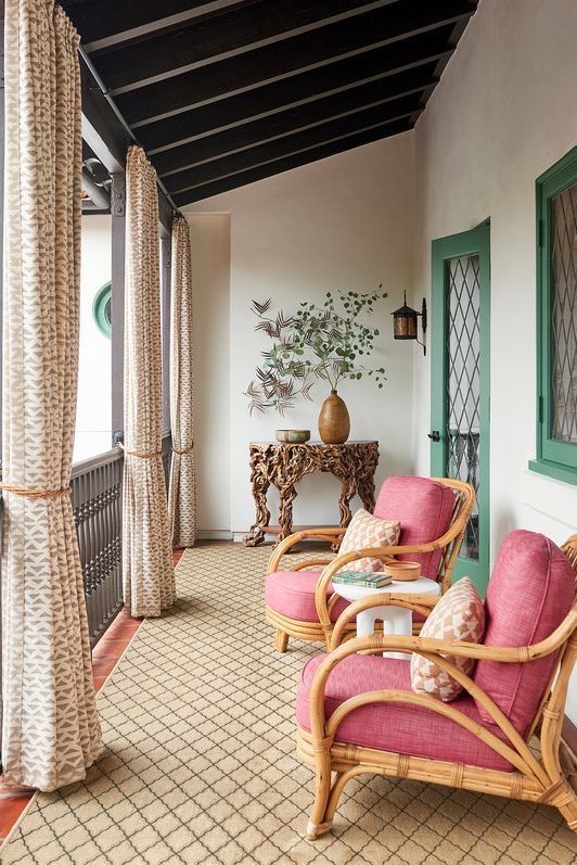 a refined porch with pink rattan chairs, curtains, a unique table with decor and a green door plus a window with a green frame