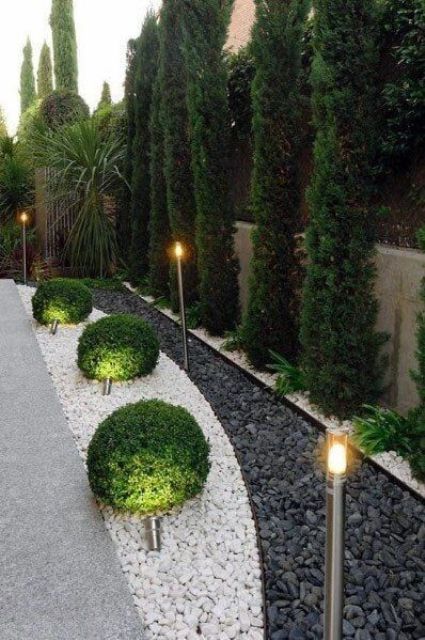 a refined space with a fence, tree trees, pebbles and topiaries plus lights is very chic and bold, great for a manicured garden