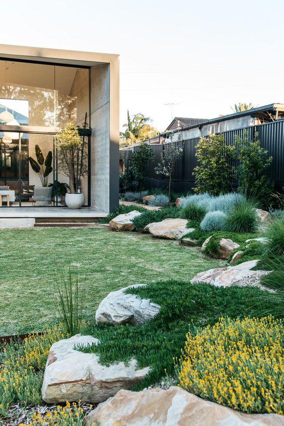 a relaxed modern garden with a green lawn, large rocks covered with grasses and some blooms is ultimate