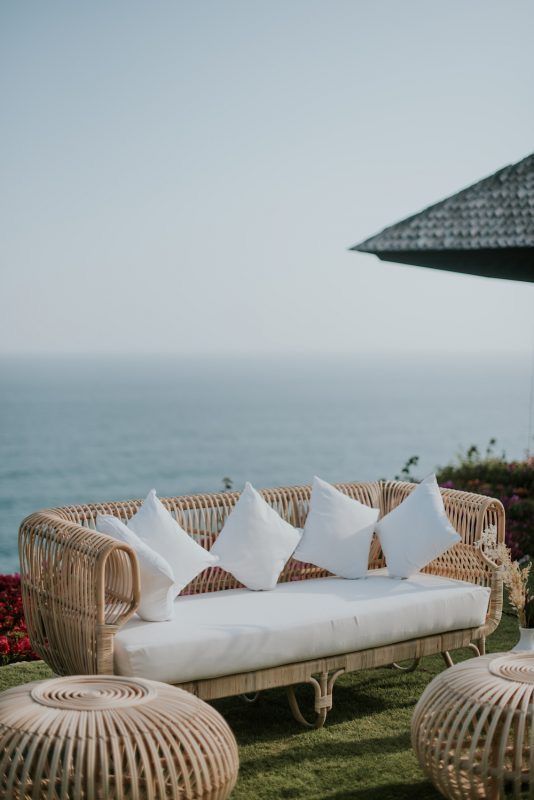 a seaside terrace with rattan furniture, neutral pillows, a coffee table and a gorgeous sea view