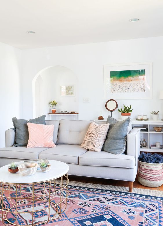 a serene coastal living room with a bright boho rug, a grey sofa with pillows, a console with decor, a coffee table and some potted plants