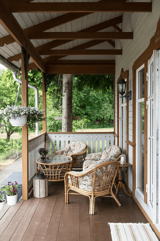 A small and pretty Scandinavian porch with rattan seating furniture with floral upholstery, a round rattan table and some blooms is summer ready