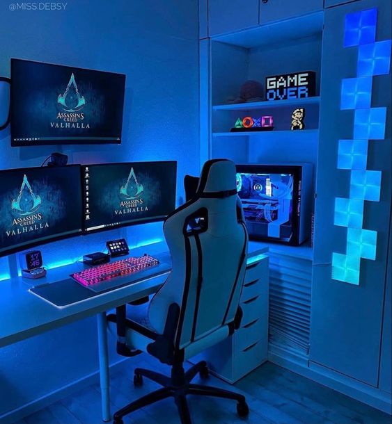 a small blue gaming setup with a desk, a PC, a chair, three screens, decor on the shelves and blue neon lights is wow