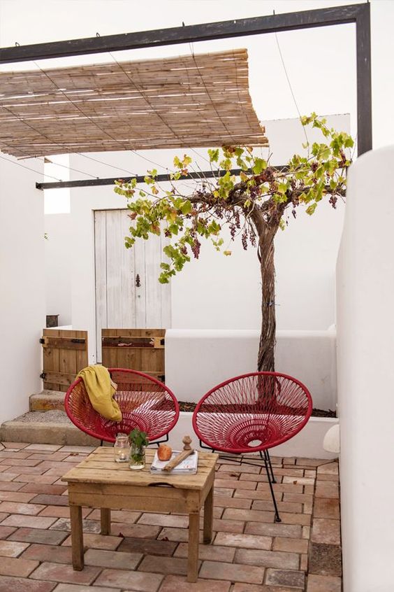 a small inner courtyard with red chairs and a yellow blanket, a reclaimed wooden table, a tree is a cool and relaxing space