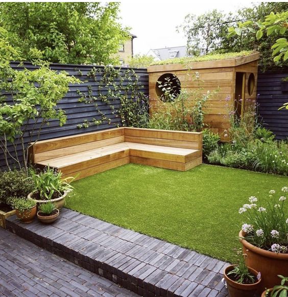 a small modern garden with a green lawn, a stained bench, some greenery and blooms around