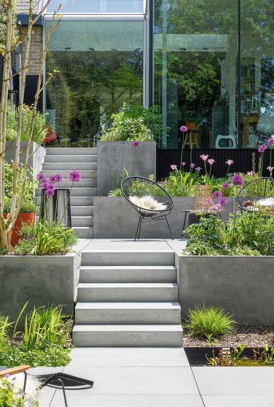 a small multi-level modern garden with some outdoor furniutre, greenery and blooms around is a cool space