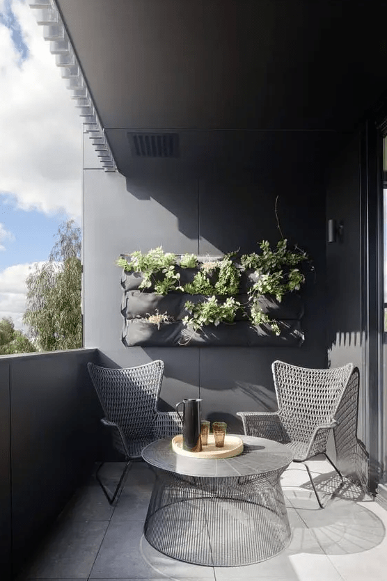 a stylish balcony with grey walls, woven chairs, a cool round table and potted greenery is a laconic and bold space to enjoy