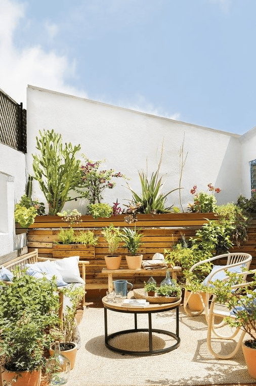 a summer space with a wooden wall, rattan furniture and lots of potted greenery and blooms for a garden feel
