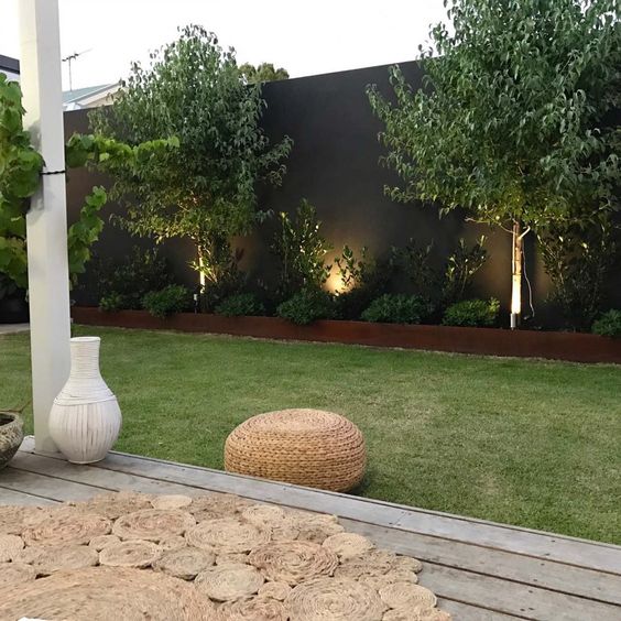 a tall black fence with a raised garden bed, shrubs, trees and greenery plus lamps are a cool and stylish modern combo