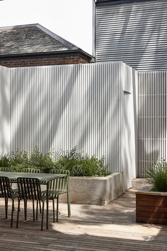a tall white fence paired with a concrete raised garden bed with greenery and grasses are a cool idea for a modern space
