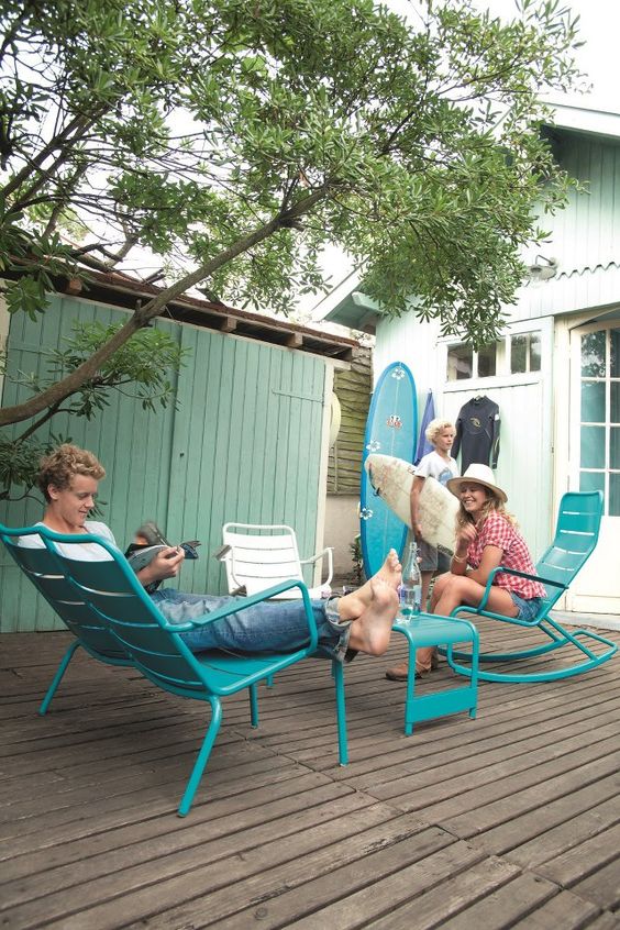 a terrace styled with turquoise chairs and a table, a tree and some surf boards is amazing