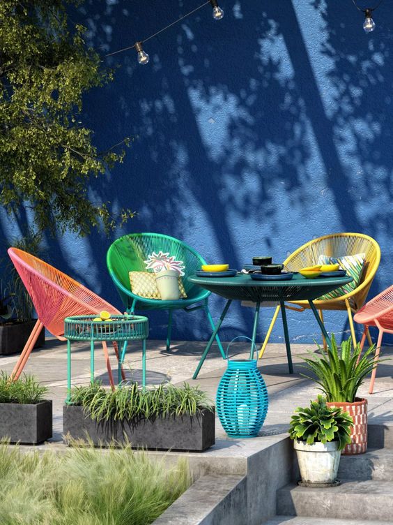 a terrace with a navy wall, colorful chairs, a green wicker table, a side table and a turquoise lantern