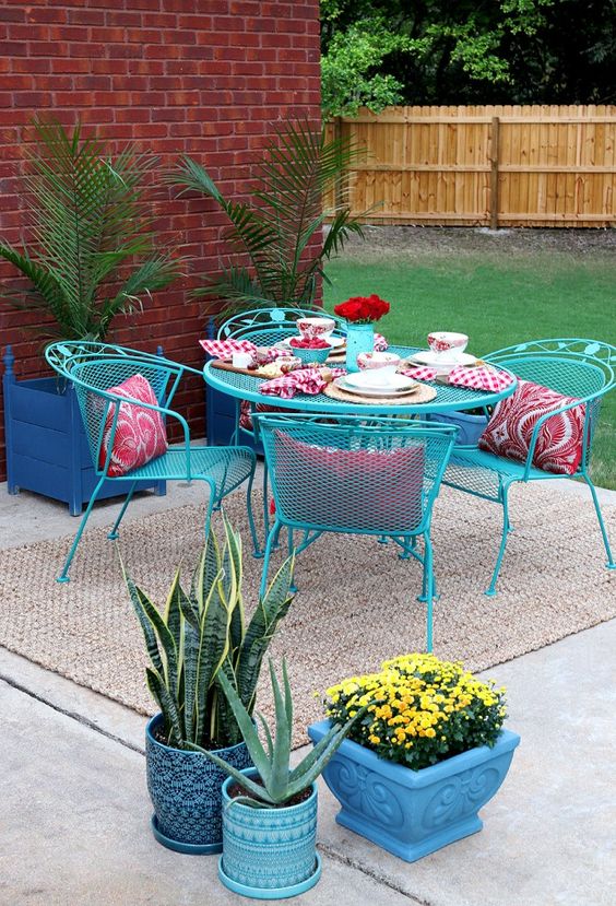a terrace with blue metal chairs and a table, navy planters with plants and blooms, pink pillows and a jute rug