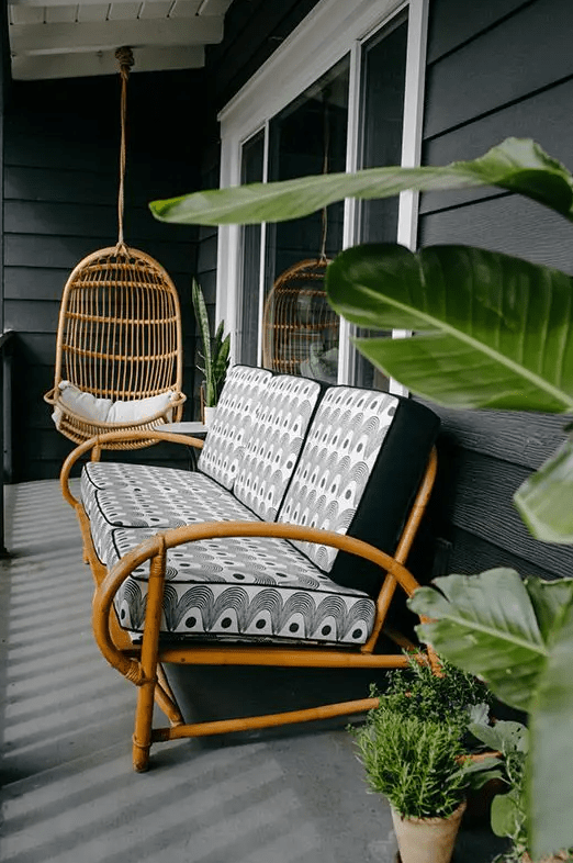 a tropical porch with a rattanegg-shaped suspended chair and a rattan sofa with printed cushions plus greenery around