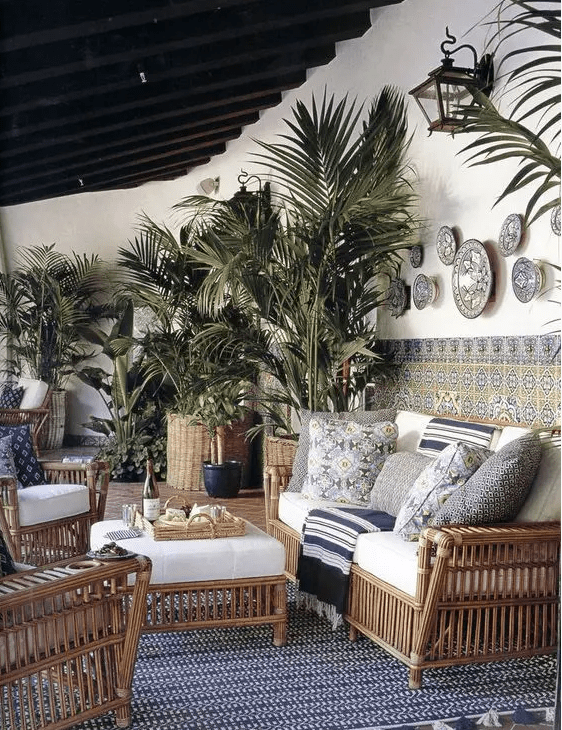 a tropical terrace with rattan furniture, printed pillows and blankets, potted plants, mosaic tiles, a printed rug and some lamps
