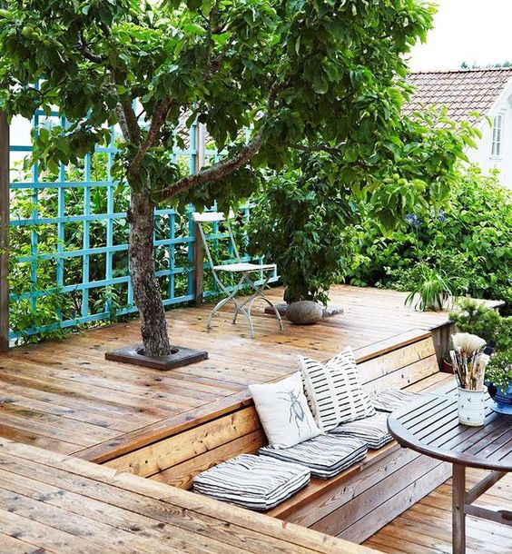 a two-level deck with trees and modern wooden furniture plus lush greenery around