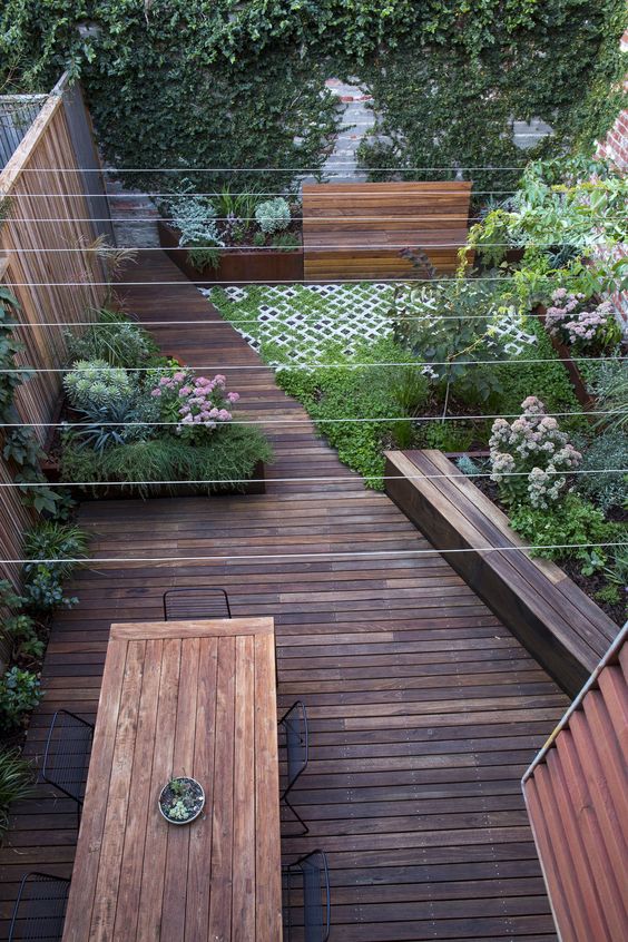 a two-level outdoor space with a deck and dining furniutre, a garden part with greenery, blooms and a bench