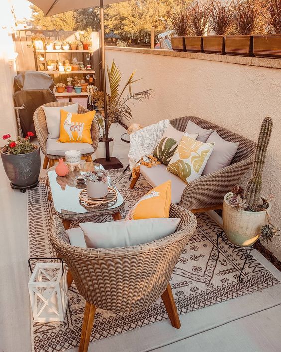 a welcoming boho terrace with wicker furniture, a boho rug and pillows, potted plants, an umbrella and a shelving unit