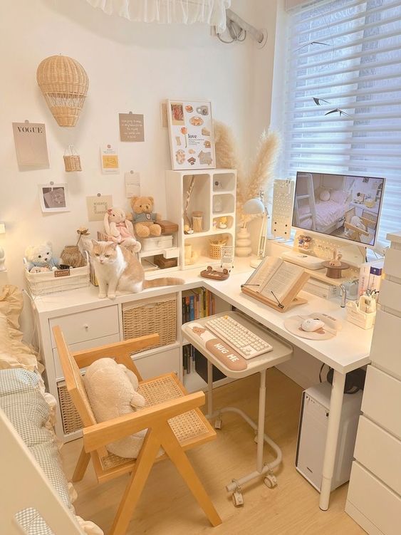a white gaming desk setup with a corner desk, a small keyboard table, a cane chair, some plush toys, pampas grass and lovely decor