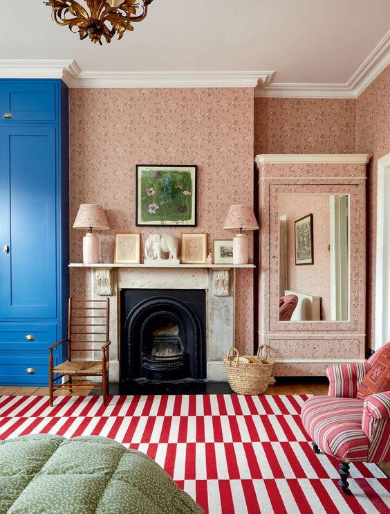 an English cottage living room with a blue wardrobe, a fireplace, a striped rug and chair, pretty pink floral wallpaper