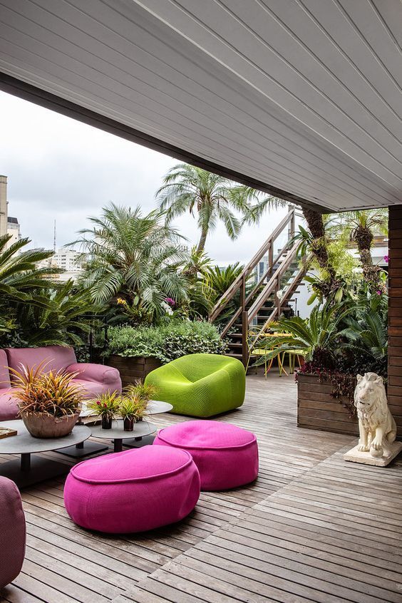 an amazing outdoor living room with a pink sofa and hot pink poufs, a green chair, metal tables and lots of tropical plants