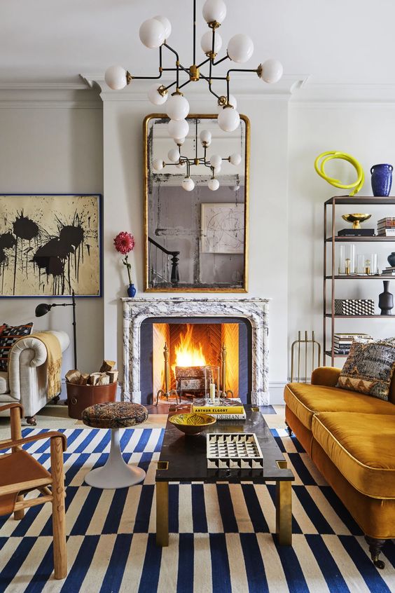 an eclectic living room with a fireplace, a mustard sofa, some chairs, a coffee table, a fireplace, a mirror and a shelving unit in the corner