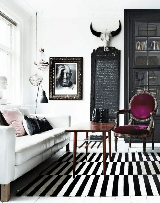 an eclectic living room with a white sofa, a stained table, a purple chair, a striped rug and a black bookcase is wow