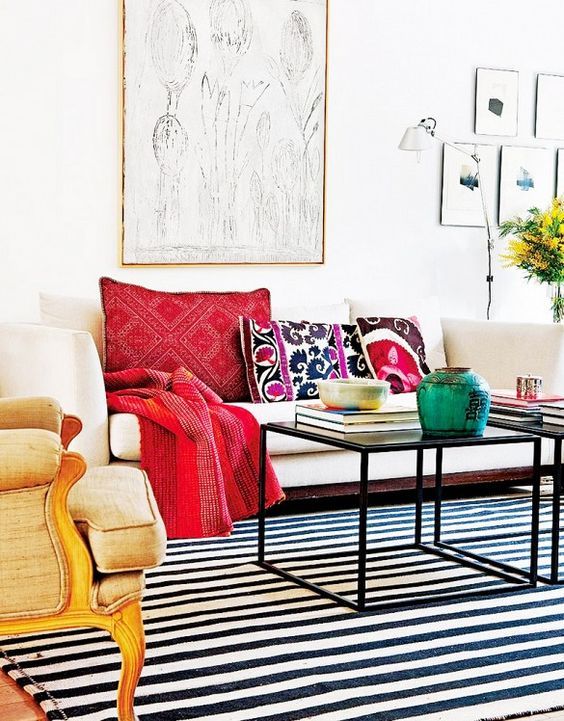 an eclectic living room with a white sofa, printed pillows, a neutral chair, coffee tables, stripe rug, a gallery wall and blooms
