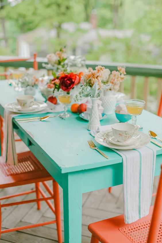 an outdoor dining space with an aqua table, coral chairs and some chic teware and blooms is amazing to have a meal here