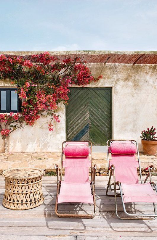 an outdoor space with pink lounge chairs, a rattan side table and some blooms on the wall is amazing