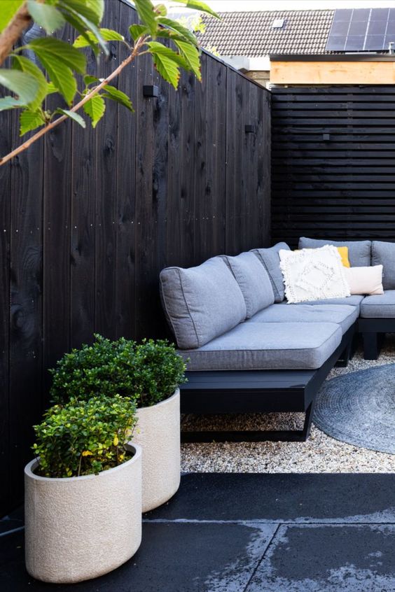 black fence and a screen, a black sofa with grey upholstery, potted greenery and some rugs for a modern space
