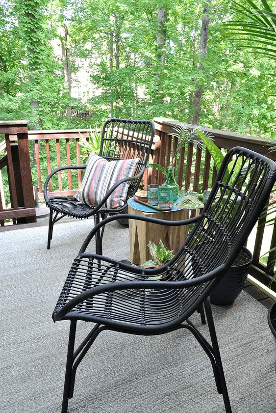 black rattan chairs, a tree stump stool with drinks and some greeneyr around to organize a cool outdoor sitting space