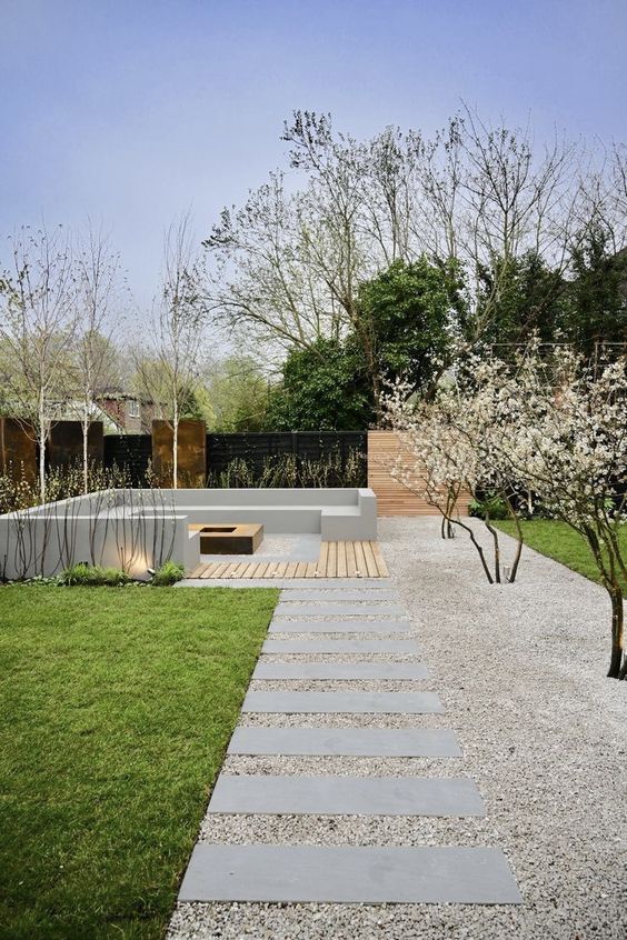 modern to minimalist garden landscaping with a green lawn, some blooming branches and trees, a concrete bench and spotlights