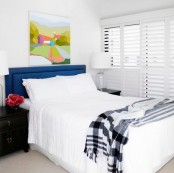 a neutral bedroom with a touch of color – a navy headboard, a black nightstand, a colorful artwork, looks larger and bolder