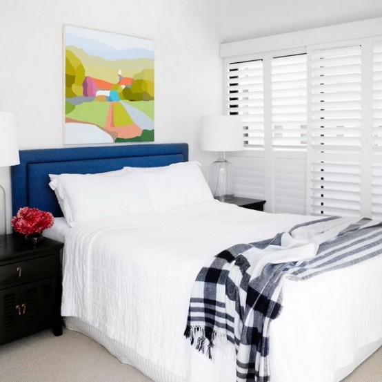 a neutral bedroom with a touch of color - a navy headboard, a black nightstand, a colorful artwork, looks larger and bolder