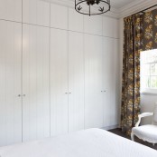 a small bedroom with white on white decor and a contrasting floor and dark floral curtains for a bold contrast