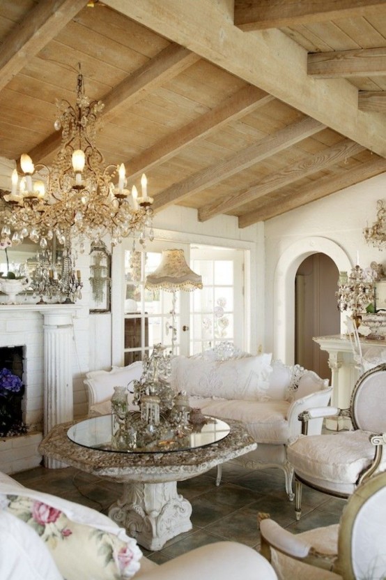 an exquisite Provence living room with wooden beams on the ceiling, a refined fireplace, a crystal chandelier and a mirror table