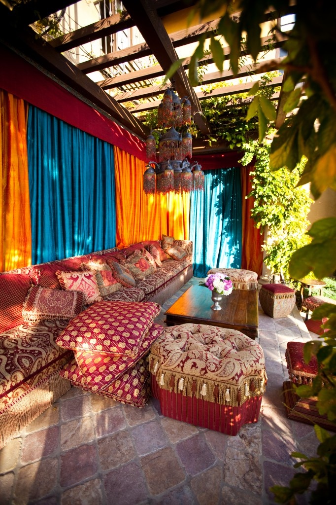A colorful Morocco style boho terrace with turquoise and orange curtains, soft seating furniture with bright upholstery, potted greenery