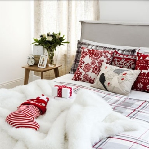 a neutral bedroom spruced up for Christmas with red and white bedding, a faux fur rug and a striped stocking on the bed