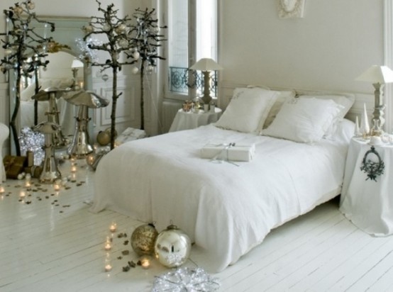 a white Christmas bedroom with quirky trees decorated with sheer and silver ornaments, candles, lamps and oversized ornaments on the floor