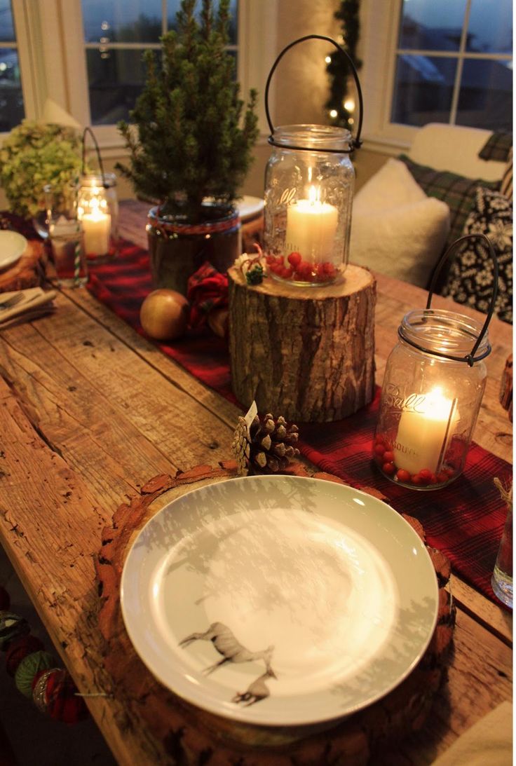 A rustic Christmas tablescape with a red burlap ribbon, candle lanterns, a mini tree and tree stump, wood slice placemats and pinecones all over