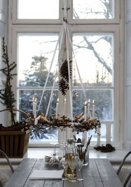 a vine chandelier with greenery, candles and pinecones, a Christmas tree in a crate for a chic Nordic rustic feel in the space