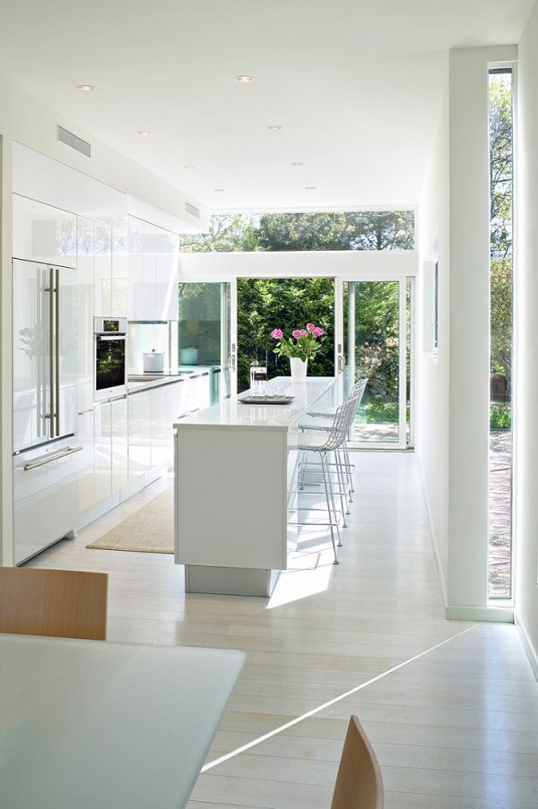 A modern all white kitchen with a glazed wall with sliding doors that open the kitchen and dining zone to outdoors