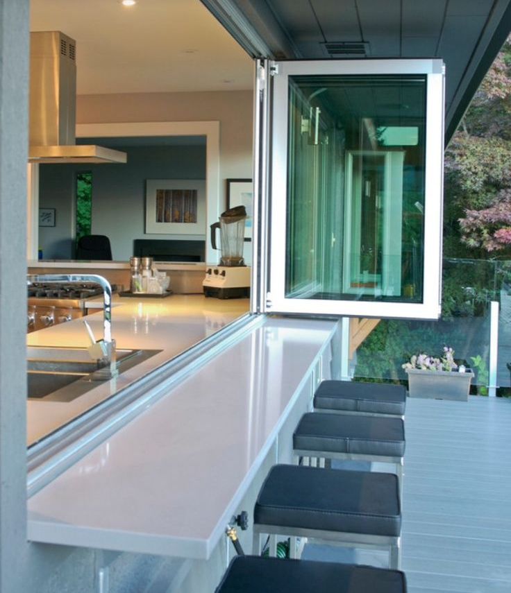 A neutral modern kitchen with a pass through window that is folding and tall stools outdoors for indoor outdoor meals