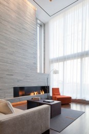 a double-height minimalist living room with a wood clad fireplace wall, contemporary furniture and a large window for more natural light