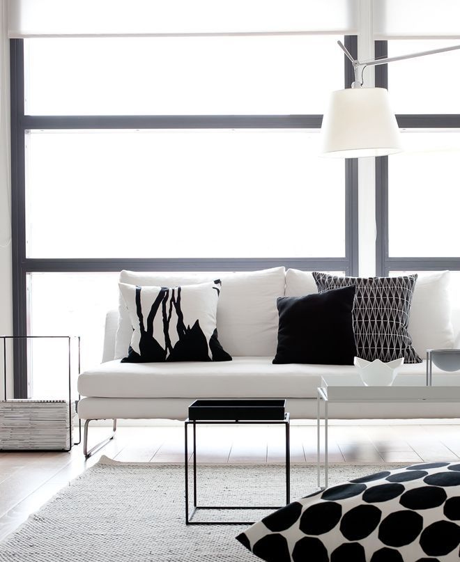 A minimalist black and white living room with a stylish white couch, printed black and white pillows plus coffee tables