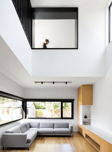 A minimalist double height living room with a grey sectional sofa, neutral wooden furniture, windows to flood the space with light