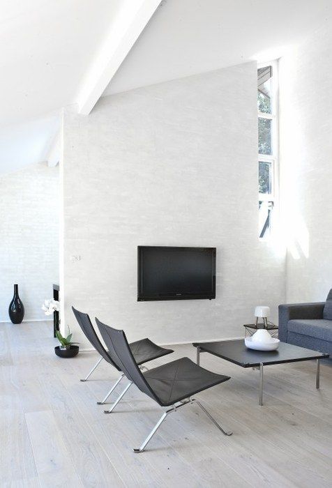 a white minimalist living room with a TV, windows, black and grey furniture that looks comfortable and cozy