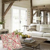 a neutral farmhouse living room with white and wooden furniture, wooden beams and colorful pillows plus greenery