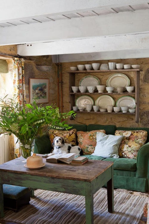 a rustic living room with a green sofa, some shabby chic and rustic furniture and potted greenery